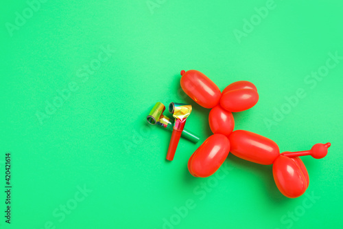 Party blowers and dog figure made of modelling balloon on green background, flat lay. Space for text