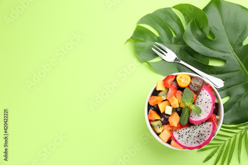 Delicious exotic fruit salad on green background, flat lay. Space for text