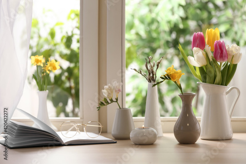 Different beautiful spring flowers, burning candle and book on window sill