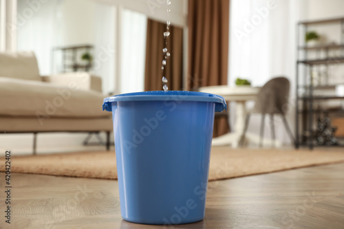 Bucket collecting water from ceiling in living room. Leaking roof