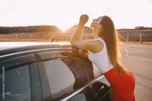 Beautiful young girl near a car in the evening in the sunset sun in an empty parking lot © Daria Lukoiko