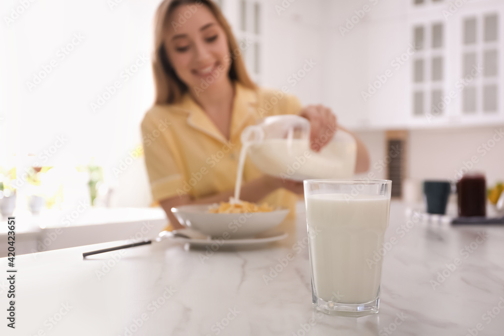 Woman with gallon bottle and breakfast cereal at white marble table in kitchen, focus on glass of milk Woman with gallon bottle and breakfast cereal at white marble table in kitchen, focus on glass of milk