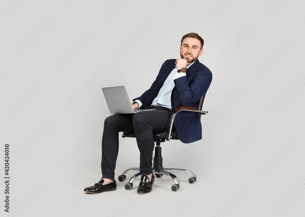 Young businessman with laptop sitting in comfortable office chair on grey background Young businessman with laptop sitting in comfortable office chair on grey background