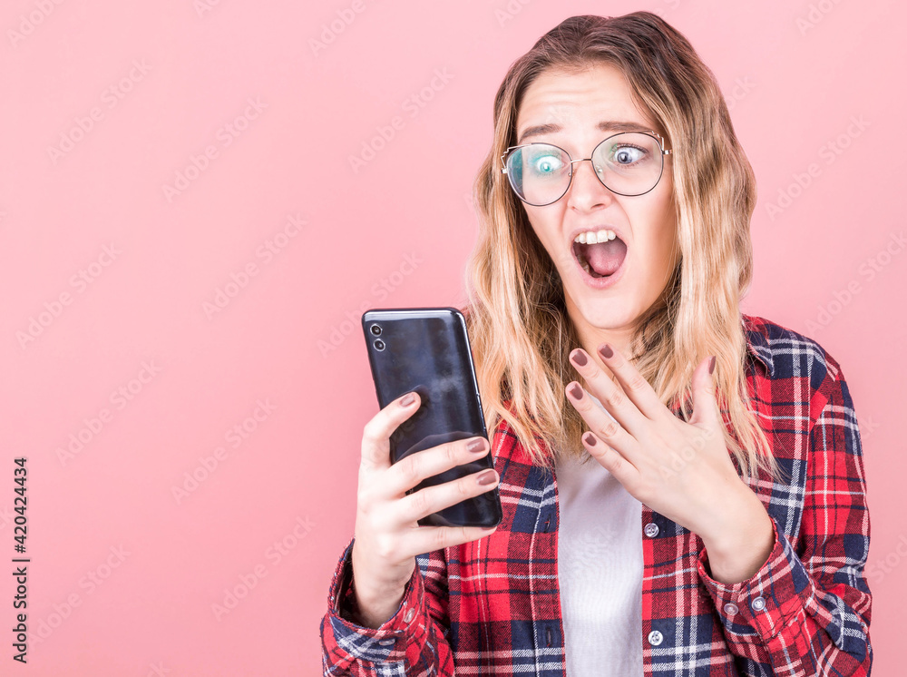 Portrait of a shocked young girl using mobile phone isolated over pink background Portrait of a shocked young girl using mobile phone isolated over pink background