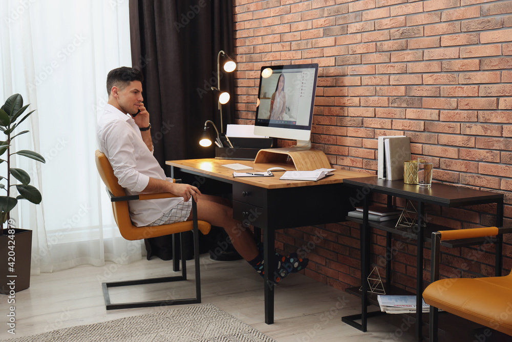 Businessman in shirt and underwear talking on mobile phone near computer at home office