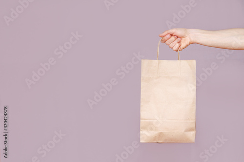 Male hand holding paper bag on light background with copy space