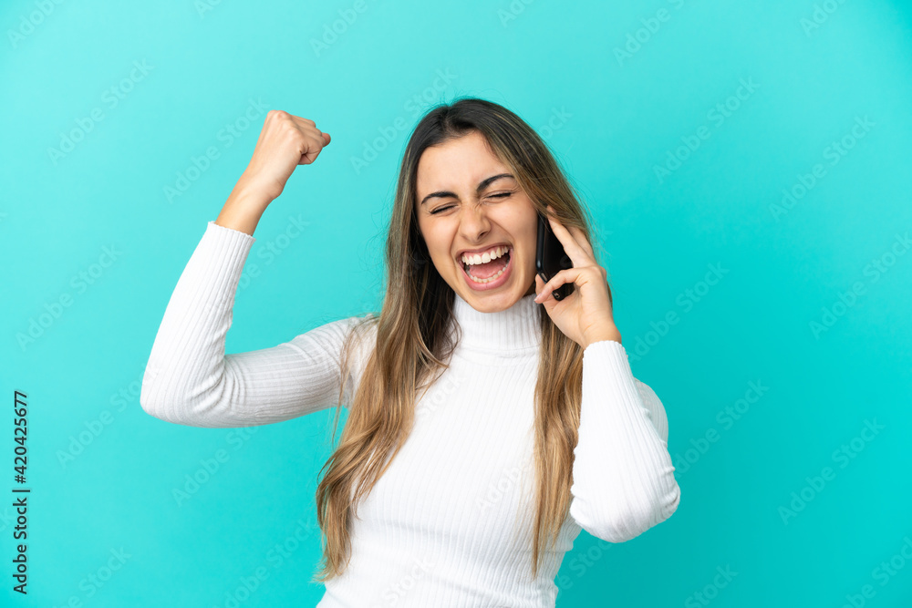 Young caucasian woman using mobile phone isolated on blue background celebrating a victory Young caucasian woman using mobile phone isolated on blue background celebrating a victory