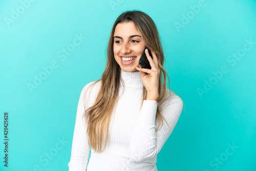 Young caucasian woman using mobile phone isolated on blue background looking side