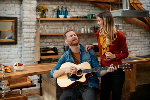 Young couple enjoying while playing acoustic guitar and drinking wine at home.