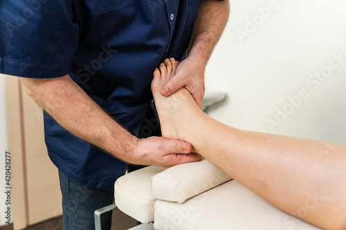 Doctor specialized in osteopathy in the medical clinic performs manipulations and massages to the young woman patient with his hands acting on the foot for various physical ailments photo