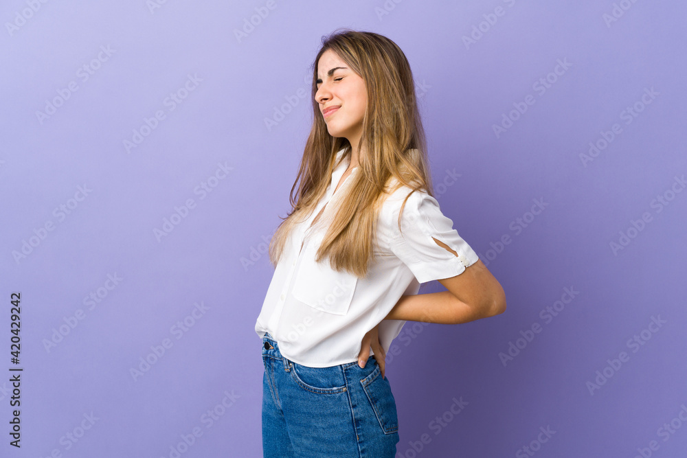Young woman over isolated purple background suffering from backache for having made an effort Young woman over isolated purple background suffering from backache for having made an effort