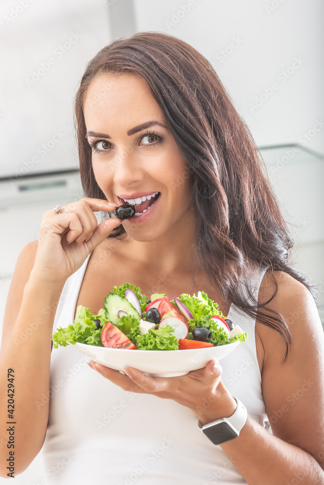 Beautiful woman biting into an olive taken from a healthy salad in her other hand Beautiful woman biting into an olive taken from a healthy salad in her other hand