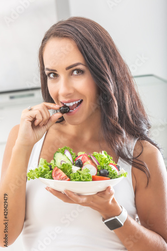 Beautiful woman biting into an olive taken from a healthy salad in her other hand