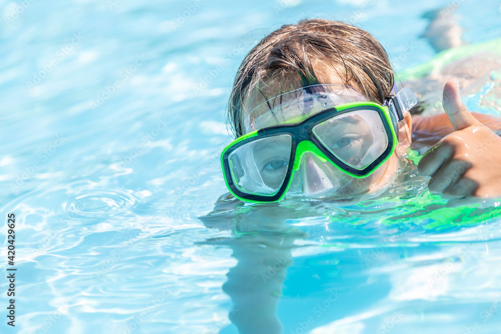 Child swimming in a pool with goggles on showing thumbs up gesture