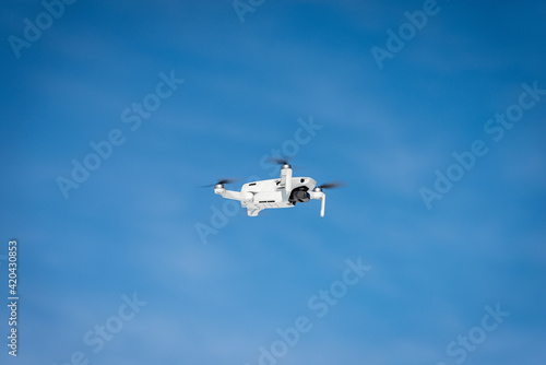 Small white drone flying on blue sky with clouds and copy space, photography.