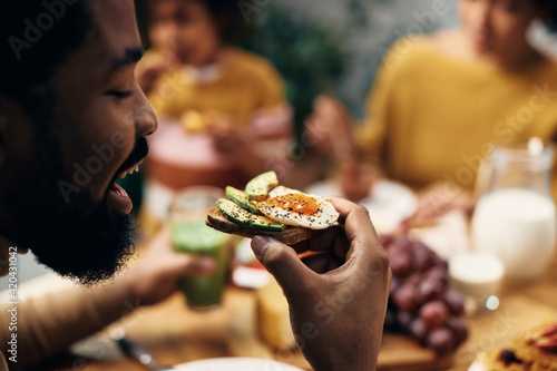 Fototapeta Close-up of black  man eating healthy sandwich at home.