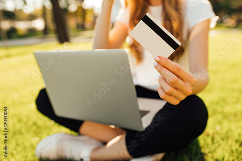 Young woman holding credit card and using laptop sitting on the lawn in the park © Shopping King Louie