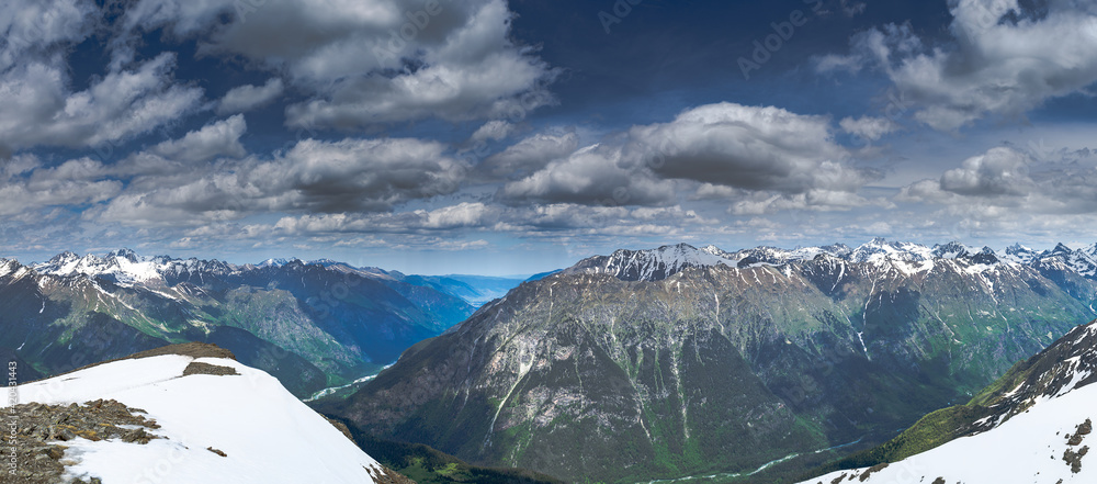 A wide panorama of the mountain peaks of the Caucasian ridge with gloomy heavy clouds