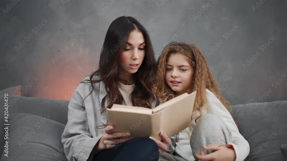 Beautiful mother and her daughter are reading books while sitting on the couch at home Beautiful mother and her daughter are reading books while sitting on the couch at home