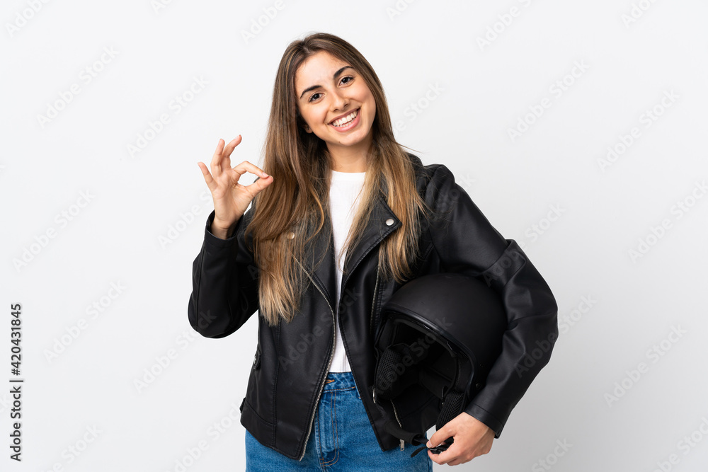 Young Woman holding a motorcycle helmet over isolated white background showing an ok sign with fingers Young Woman holding a motorcycle helmet over isolated white background showing an ok sign with fingers