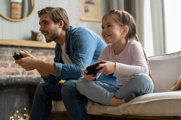 family, gaming and entertainment concept - happy father and little daughter with gamepads playing video game at home.