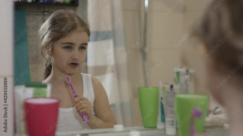 Close-up Portrait Young Little Girl Dancing Singing With Toothbrush in Bathroom Looking at Mirror Reflection. Daily Routine Dental Hygiene. Happy Portrait Caucasian Toothless Child Dancing in Bathroom Close-up Portrait Young Little Girl Dancing Singing With Toothbrush in Bathroom Looking at Mirror Reflection. Daily Routine Dental Hygiene. Happy Portrait Caucasian Toothless Child Dancing in Bathroom