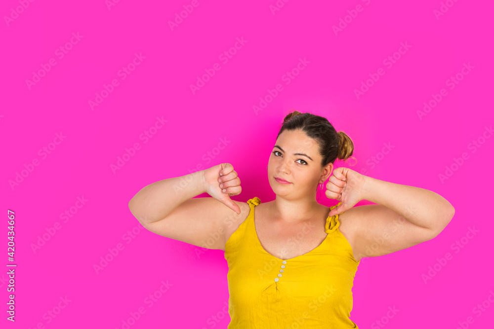 Mujer joven haciendo un gesto de pesimismo con los pulgares hacia abajo sobre un fondo fucsia liso y aislado. Vista de frente. Copy space Mujer joven haciendo un gesto de pesimismo con los pulgares hacia abajo sobre un fondo fucsia liso y aislado. Vista de frente. Copy space