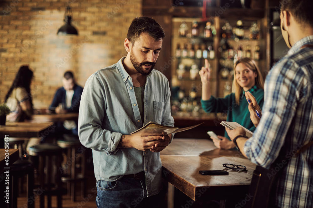 Obraz premium Young man reading menu while making order in a pub.