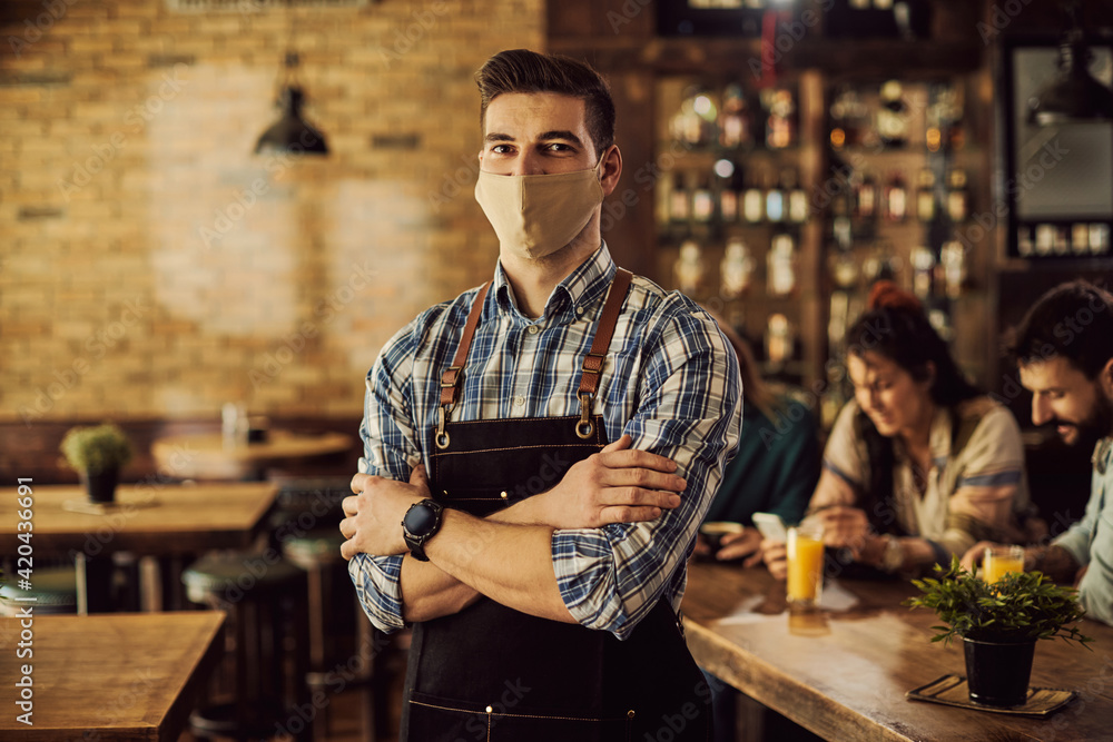 Portrait of confident waiter wearing face mask in a cafe due to coronavirus pandemic. Portrait of confident waiter wearing face mask in a cafe due to coronavirus pandemic.