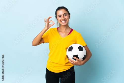 Young hispanic football player woman over isolated on blue background showing ok sign with fingers © luismolinero