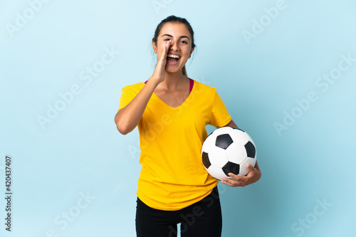 Young hispanic football player woman over isolated on blue background shouting with mouth wide open © luismolinero