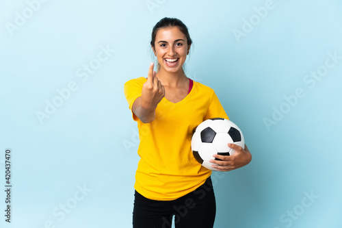 Young hispanic football player woman over isolated on blue background doing coming gesture © luismolinero
