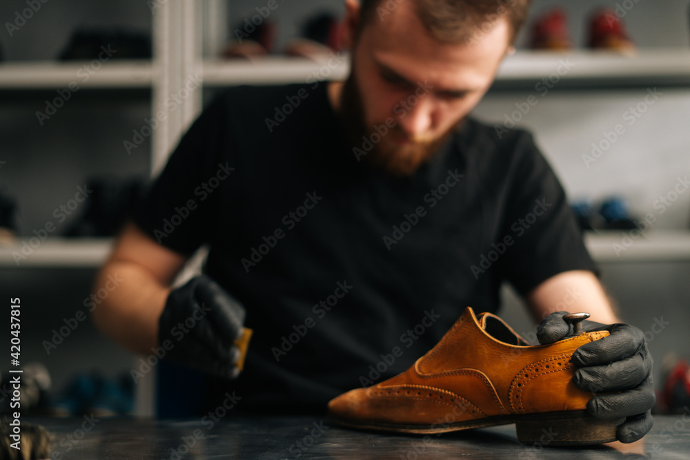 Front view of shoemaker wearing black latex gloves polishing old light brown leather shoes for later restoration. Concept of cobbler artisan repairing and restoration work in shoe repair shop. Front view of shoemaker wearing black latex gloves polishing old light brown leather shoes for later restoration. Concept of cobbler artisan repairing and restoration work in shoe repair shop.