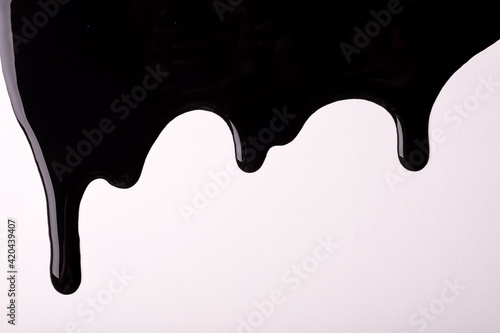 Black liquid drops of paint color flow down on isolated white background. Abstract dark backdrop with fluid drip pattern