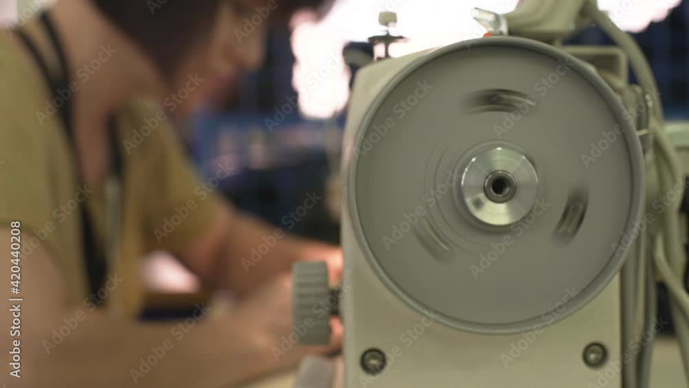 seamstress with red manicure sews bright fabric and zippers with modern machine tool at workplace in light room extreme close view seamstress with red manicure sews bright fabric and zippers with modern machine tool at workplace in light room extreme close view