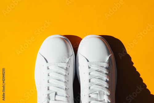 White sneakers on an orange background with hard shadows.