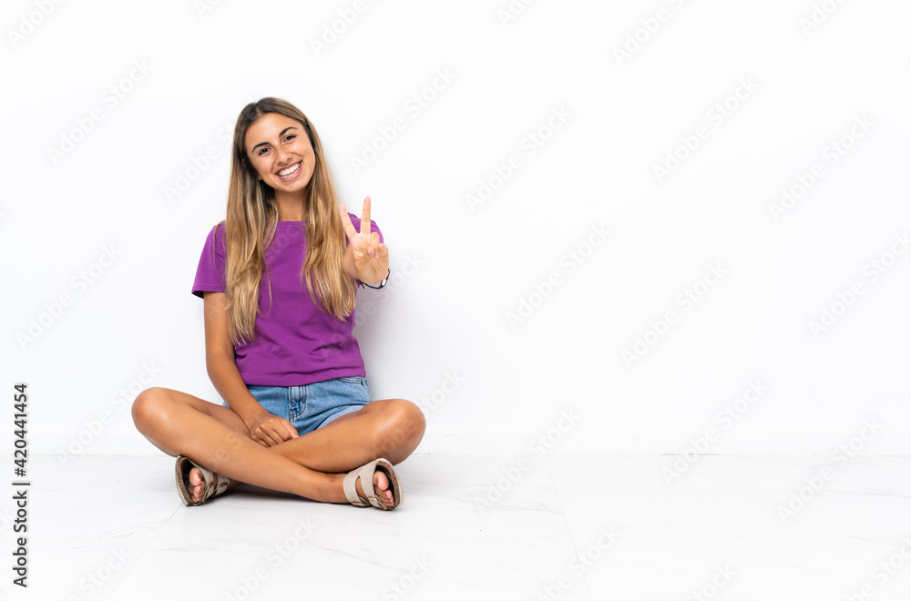 Young hispanic woman sitting on the floor smiling and showing victory sign Young hispanic woman sitting on the floor smiling and showing victory sign