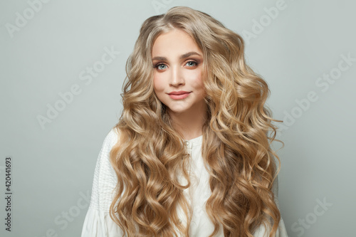 Attractive blonde woman with long perfect hair looking at camera and smiling on white background