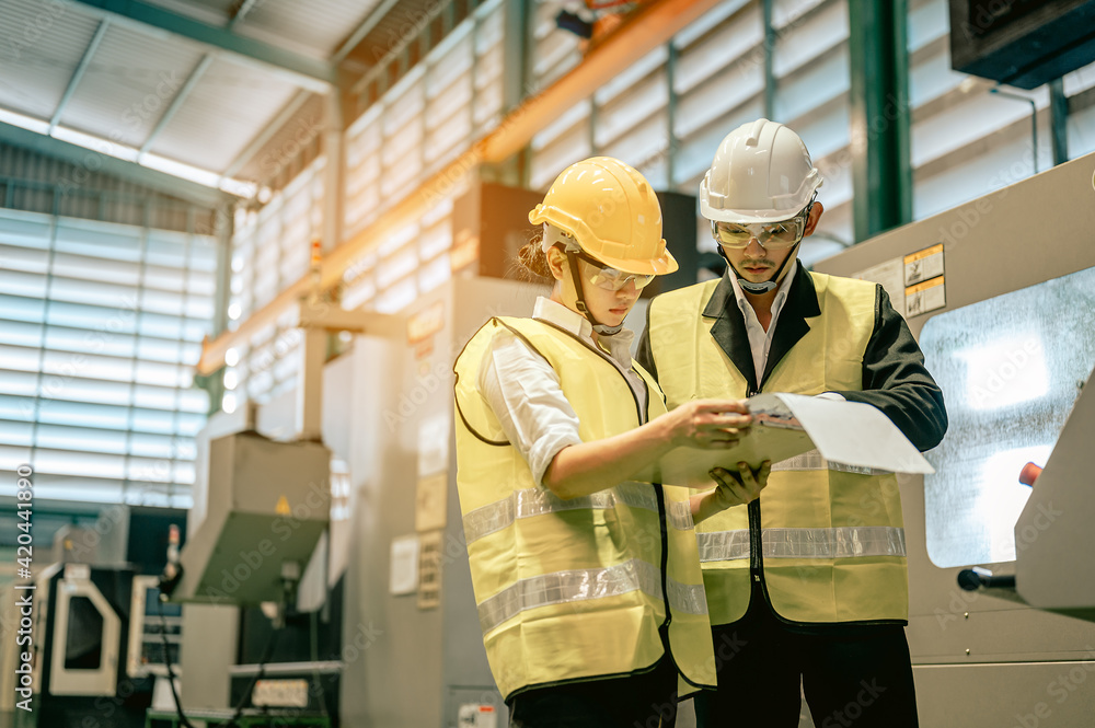 Male and female industrial engineers in hard hats discuss new project while using blue print in industry manufacturing factory.Engineer and Architect concept. Male and female industrial engineers in hard hats discuss new project while using blue print in industry manufacturing factory.Engineer and Architect concept.