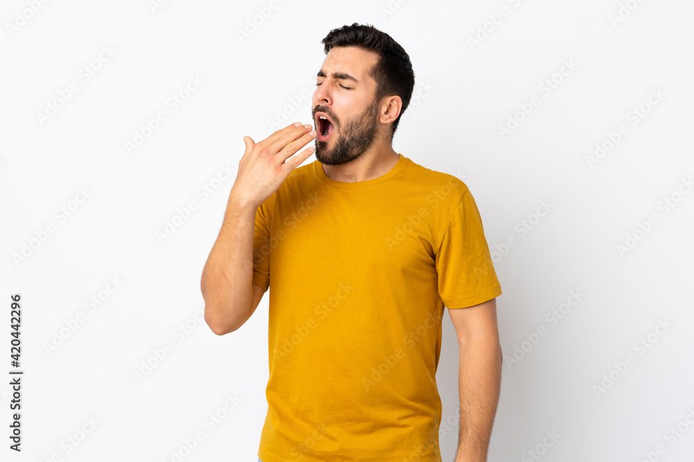 Young handsome man with beard isolated on white background yawning and covering wide open mouth with hand Young handsome man with beard isolated on white background yawning and covering wide open mouth with hand
