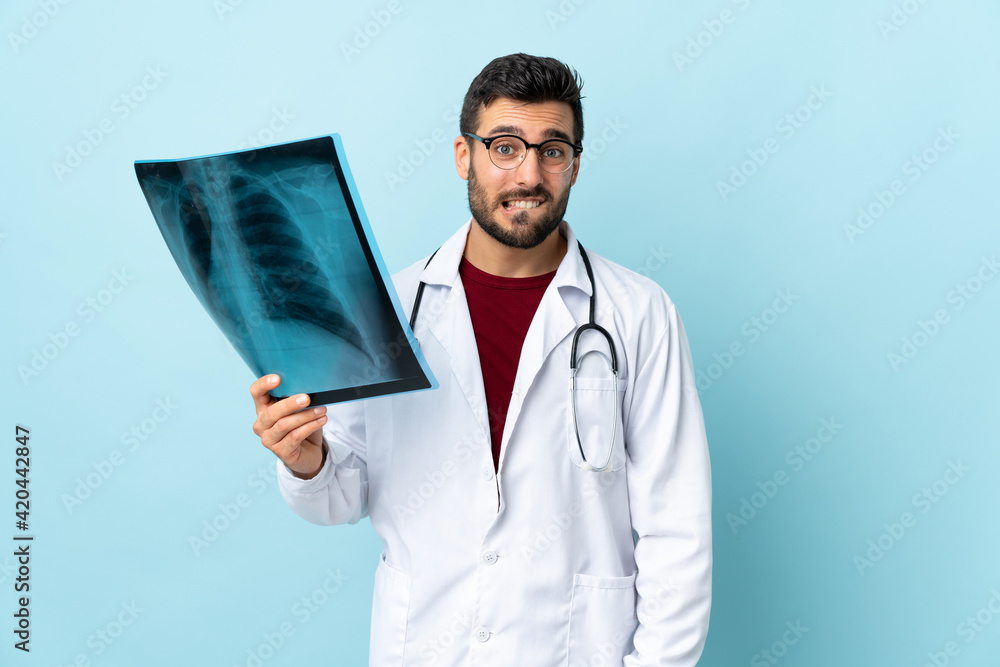 Professional traumatologist holding radiography isolated on blue background having doubts and with confuse face expression