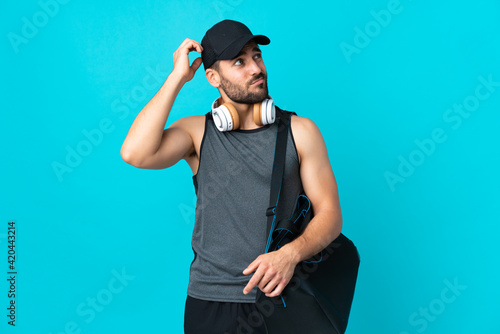 Young sport man with sport bag isolated on blue background having doubts while scratching head