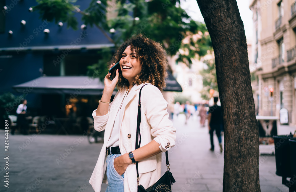 Joyful hipster girl in stylish wear connecting to internet in roaming for making international cell conversation and discuss travel journey, smiling female millennial enjoying mobile communication