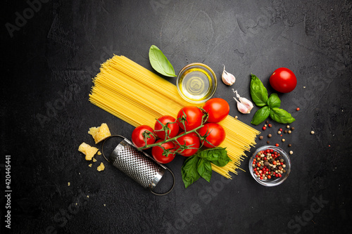 Pasta background. Several types of dry pasta with vegetables and herbs on black background. Free space for text. Top view