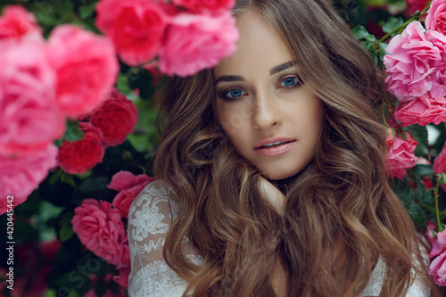 Beautiful portrait of a woman in poses. A brunette woman is standing next to roses in nature. High quality photo.