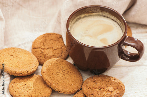 Fototapeta Naklejka Na Ścianę i Meble -  A cup of aromatic coffee cappuccino with Oatmeal cookies. Morning rays and latte for breakfast in a beautiful brown cup. Wooden background.