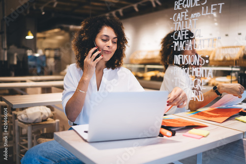 Caucaisan female student making cellphone conversation for discussing remote work in coffee shop, cafe manager with laptop computer talking about delivery details using mobile gadget for calling