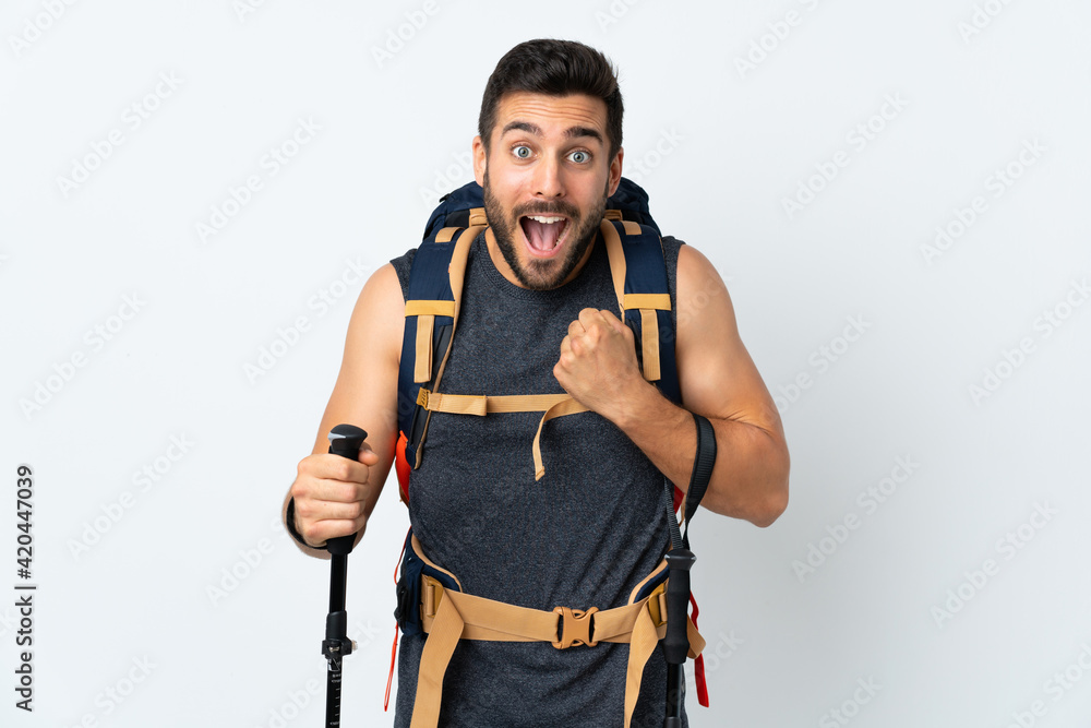 Young mountaineer man with a big backpack and trekking poles isolated on white background celebrating a victory Young mountaineer man with a big backpack and trekking poles isolated on white background celebrating a victory