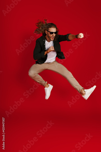 Full length of playful young man in casual clothing making a face and punching while hovering against red background