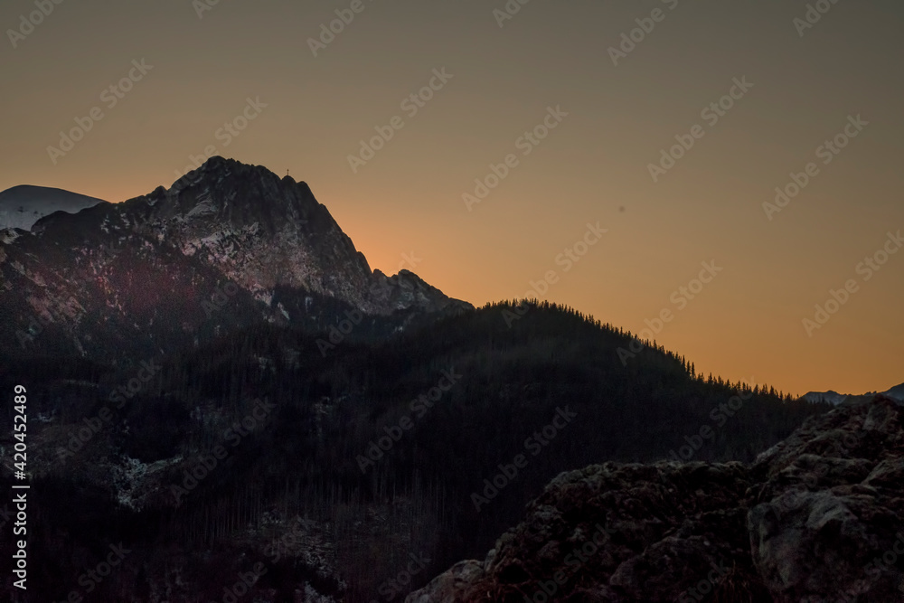 The sun is setting behind Giewont Peak - a legendary peak in Tatra Mountains, Poland. Selective focus on the rocky ridge, blurred background.